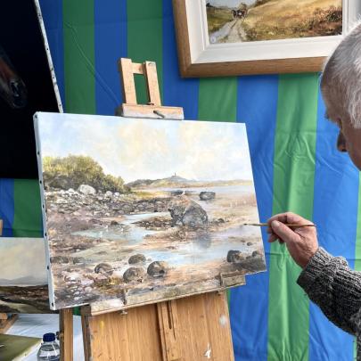 an artist paints a river scene on a canvas on an easle
