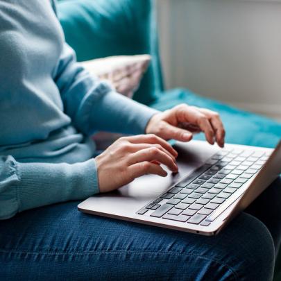 Woman sitting typing on a laptop that rests on her knee