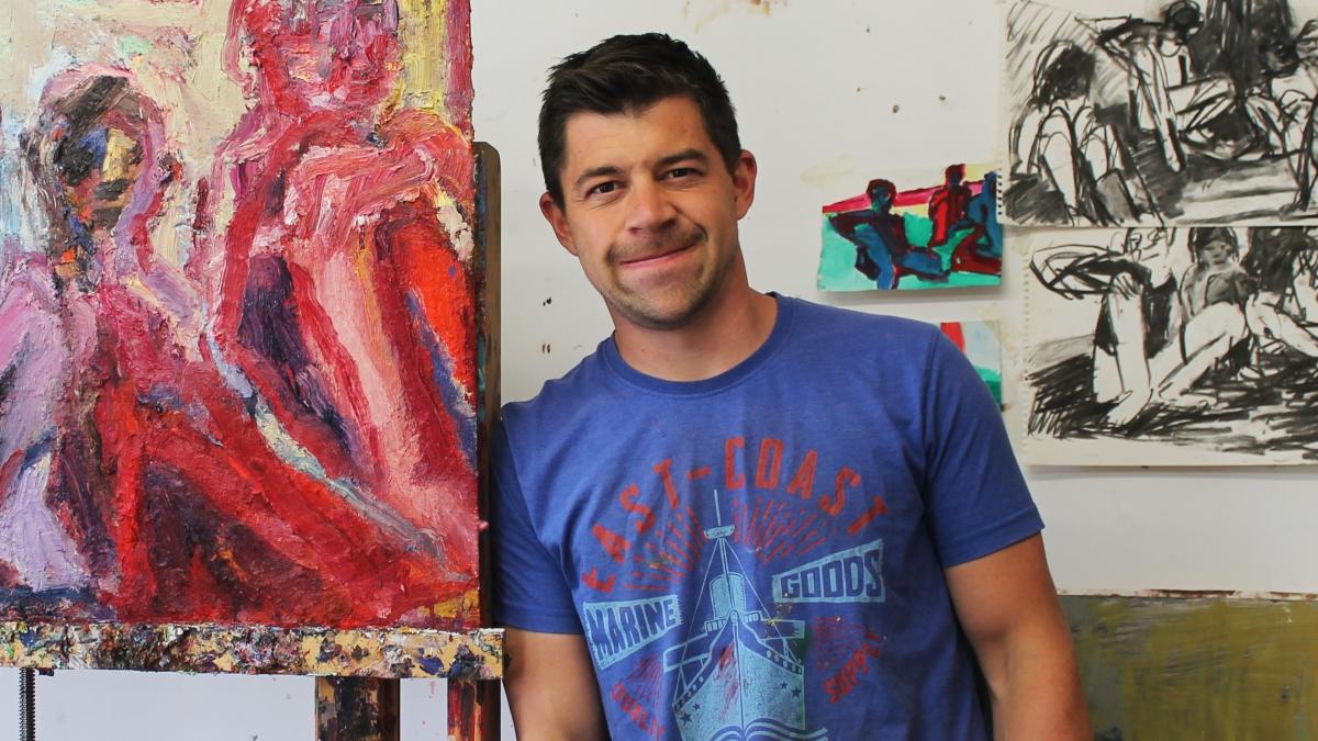 Craig Jefferson standing beside his painting on an easel in his studio